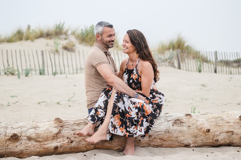 Couple complice assis sur un tronc d'arbre à la plage