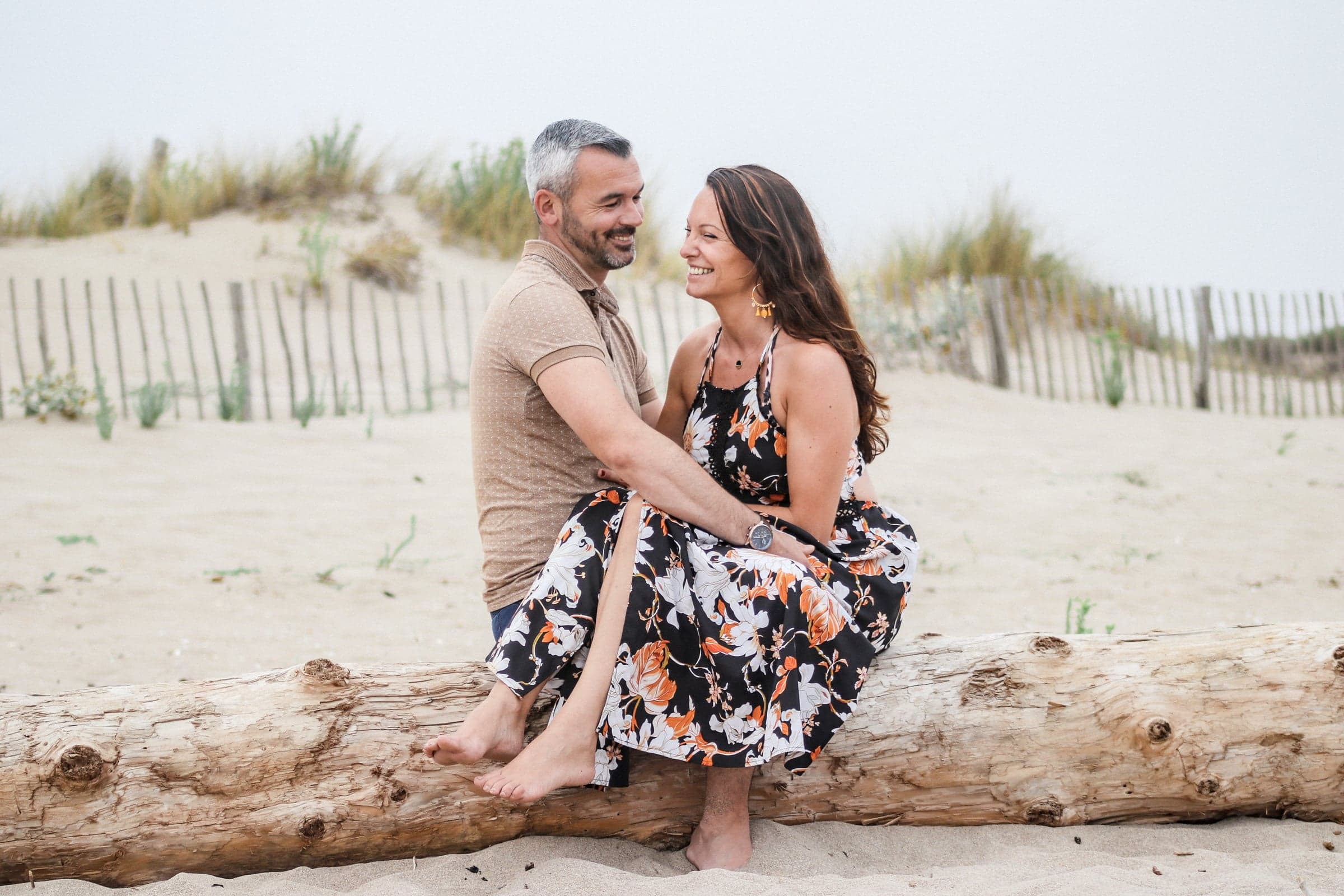 Couple complice assis sur un tronc d'arbre à la plage